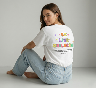 Woman wearing white Be Like Children Christian t-shirt showing colorful back graphic print with Matthew 18:3 Bible verse