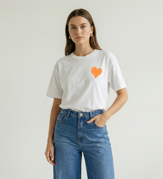 Woman standing with hand in pocket wearing white Be Like Children Christian t-shirt with orange heart graphic on front, front view portrait