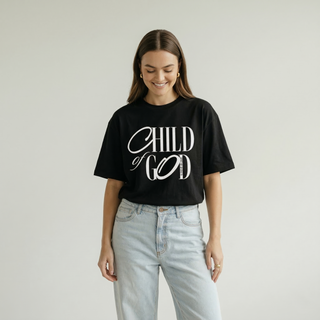 Half-body view of woman in oversized black "Child of God" Christian calligraphy tee with light denim jeans, bold faith-inspired fashion