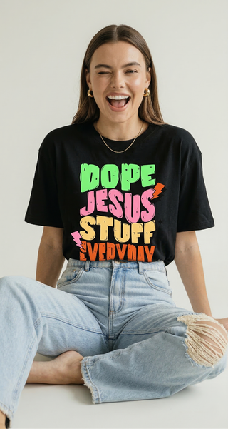 Woman wearing the Dope Jesus Tee in black, featuring colorful street-style typography that reads "Dope Jesus Stuff Everyday", sitting casually on a white floor