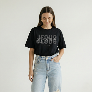 Cropped mid-body view of woman in black oversized "Jesus Saves" Luke 19:10 Christian graphic tee, hand in pocket, styled with ripped wide-leg light denim jeans