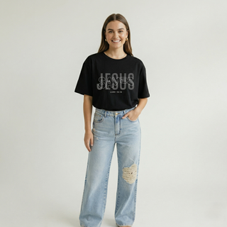 Smiling woman standing with hand in pocket in black "Jesus Saves" Luke 19:10 women's Christian faith graphic tee with layered bold design, styled with ripped wide-leg jeans