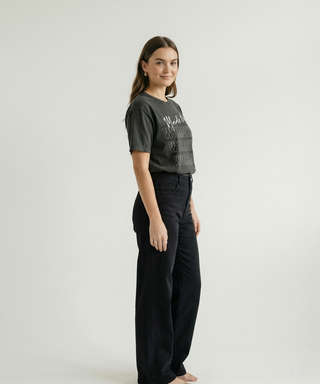Side view of woman in charcoal oversized "Made to Worship" women's faith graphic tee with WORSHIP text design, styled with black wide-leg trousers barefoot