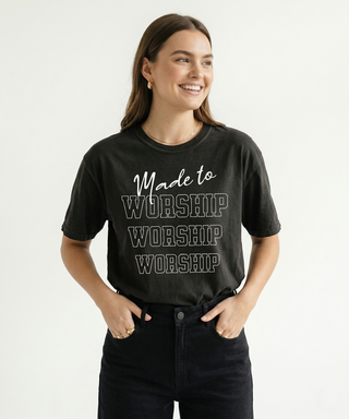 Smiling woman with both hands in pockets in dark charcoal "Made to Worship" Christian graphic tee showing bold stacked WORSHIP text design clearly