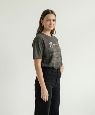 Side profile of woman with hand in pocket in dark charcoal "Made to Worship" women's Christian graphic tee with stacked WORSHIP bold text, black jeans