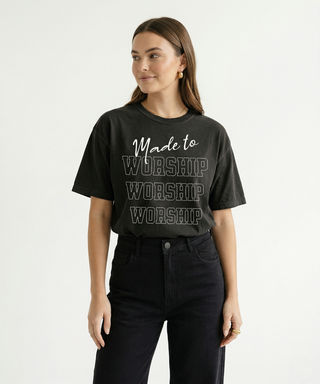 Full body view of woman in dark charcoal "Made to Worship" oversized Christian graphic tee with bold stacked WORSHIP text print, styled with black jeans