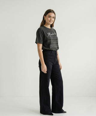 Full body side view of woman in charcoal "Made to Worship" Christian graphic tee with bold WORSHIP stacked text, styled with black wide-leg trousers