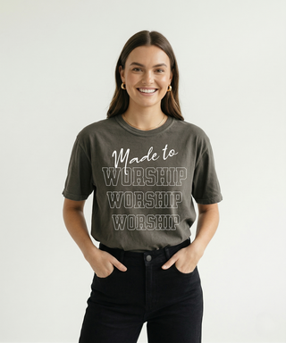 Smiling woman with hands in pockets in charcoal "Made to Worship" oversized Christian graphic tee with bold WORSHIP stacked text, black high-waist jeans