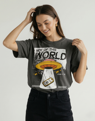 Woman posing with charcoal "Not of This World" John 17:16 UFO graphic Christian t-shirt and black pants, faith-inspired apparel