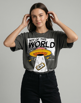 Woman styling hair while wearing charcoal "Not of This World" John 17:16 Christian streetwear t-shirt with black pants on gray background