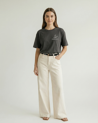 Front view of woman in charcoal gray Christian t-shirt with small Faith & Co logo, paired with wide-leg cream pants