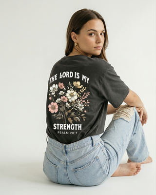 Close-up back view of Psalm 28:7 "The Lord Is My Strength" Christian graphic tee with floral design, model sitting in denim jeans