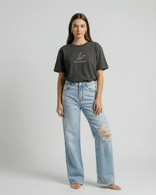 Full body front view of woman wearing Psalm 28:7 Christian graphic tee tucked into ripped blue denim jeans, casual faith-inspired outfit
